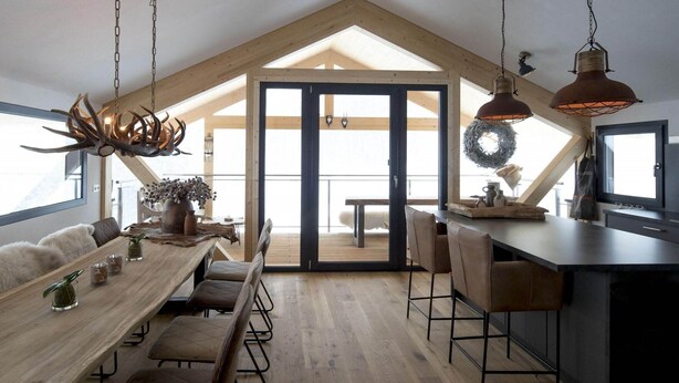 Una cocina moderna con techo de madera, un comedor con una mesa larga y sillas, y vistas a una terraza exterior a través de puertas de vidrio.