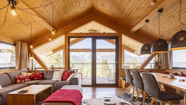 Un vaste espace de vie doté d’un plafond en bois, d’une grande porte-fenêtre coulissante donnant sur un balcon, et d’un coin repas avec une table et des chaises en bois.