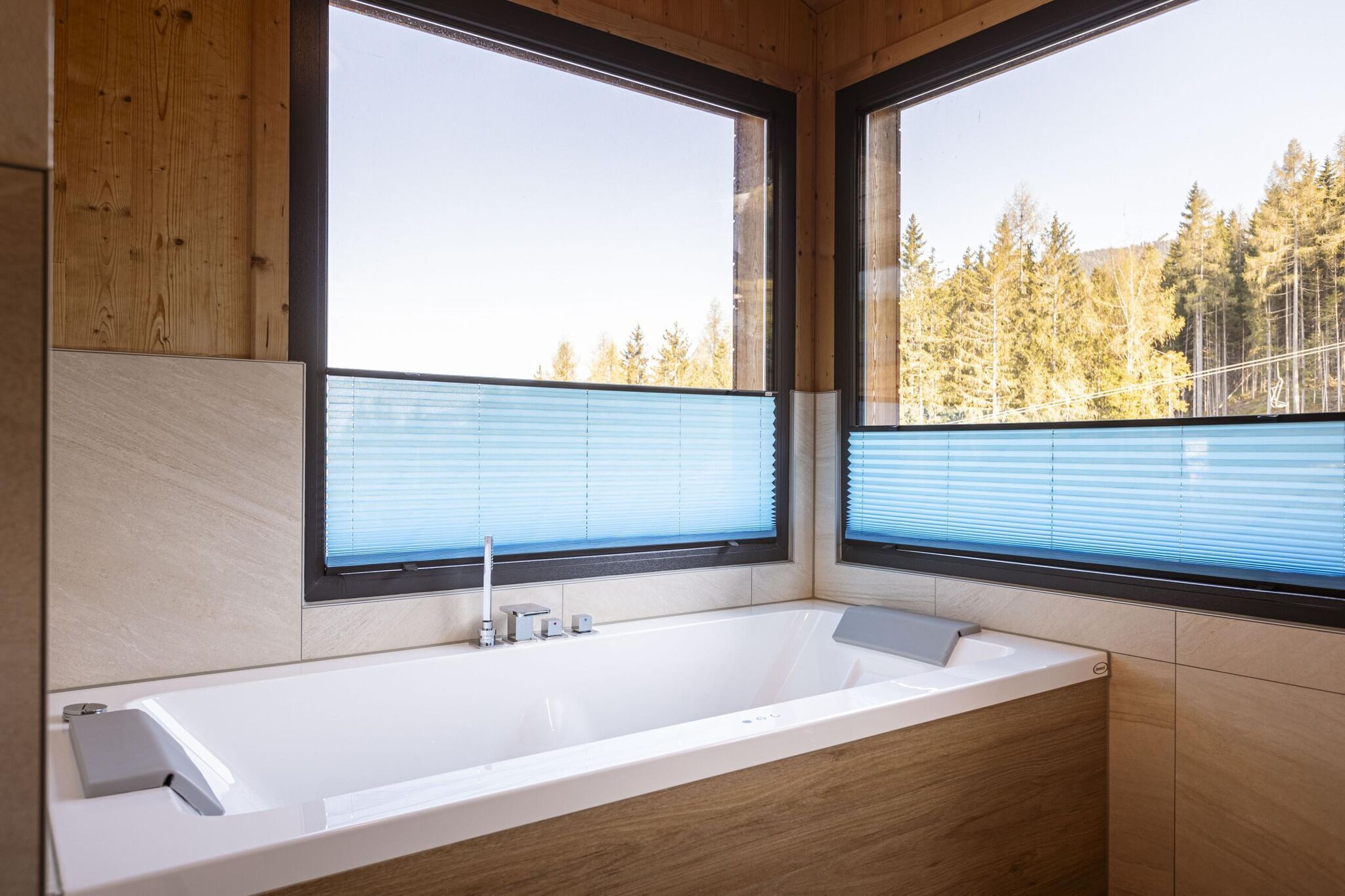 Un baño moderno con una bañera grande, paredes de madera y ventanas amplias que ofrecen vista a un área boscosa.