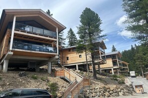 A modern multi-story building with large windows and balconies, situated on a rocky hillside with trees in the background. - Chalet with sauna on balcony (Turrach)
