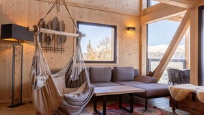 Um quarto aconchegante com rede, sofá, mesa e vista para montanhas nevadas através de grandes janelas.