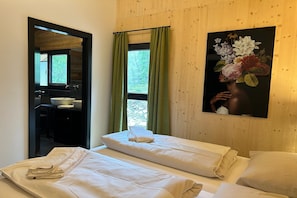 Quarto de hotel com duas camas, parede de madeira, pintura de flores e banheiro visível através de uma porta aberta.