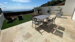 Un patio al aire libre con mesa y sillas, un área verde y vistas al mar.