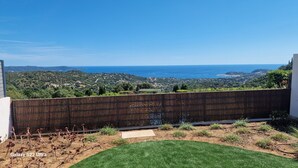 Vista desde un balcón con un paisaje costero, una valla de madera y una zona ajardinada.