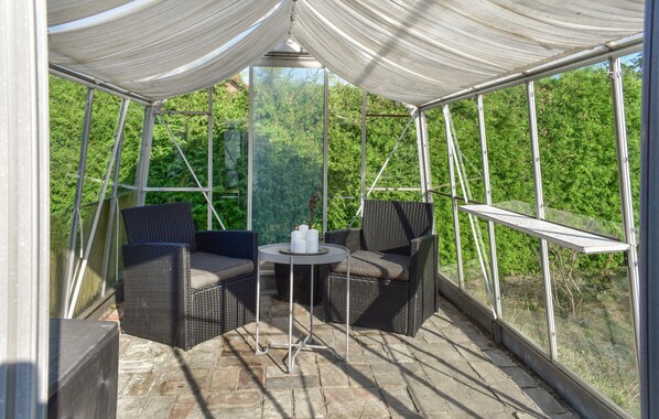 A covered outdoor seating area with wicker furniture and a small table, surrounded by glass walls and a metal frame structure. - 3 bedroom lovely home in Skivarp (Skivarp)