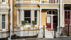 A yellow building with white trim, a balcony, and a red door. - Star Struck on Stuart Street (Dunedin)