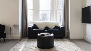 A modern living room with a black sofa, a white fur throw, a black ottoman, and a television on the wall. - Star Struck on Stuart Street (Dunedin)