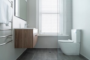 Ein modernes Badezimmer mit einem Holzkosmetikschrank, einer weißen Toilette und einem Fenster mit Jalousien.
