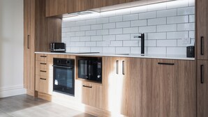 A modern kitchen with wooden cabinetry, white subway tiles, and built-in appliances including a microwave and oven. - Star Struck on Stuart Street (Dunedin)