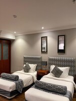 Habitación de hotel con dos camas, cada una con almohadas y cabeceros estampados, una mesita de noche con lámpara y un espejo en la pared.
