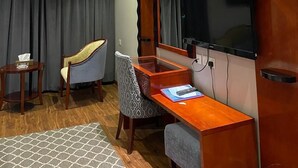 Ein Hotelzimmer mit Holzschreibtisch, Wandfernseher, Stuhl und Bett mit schwarzem Kopfteil.