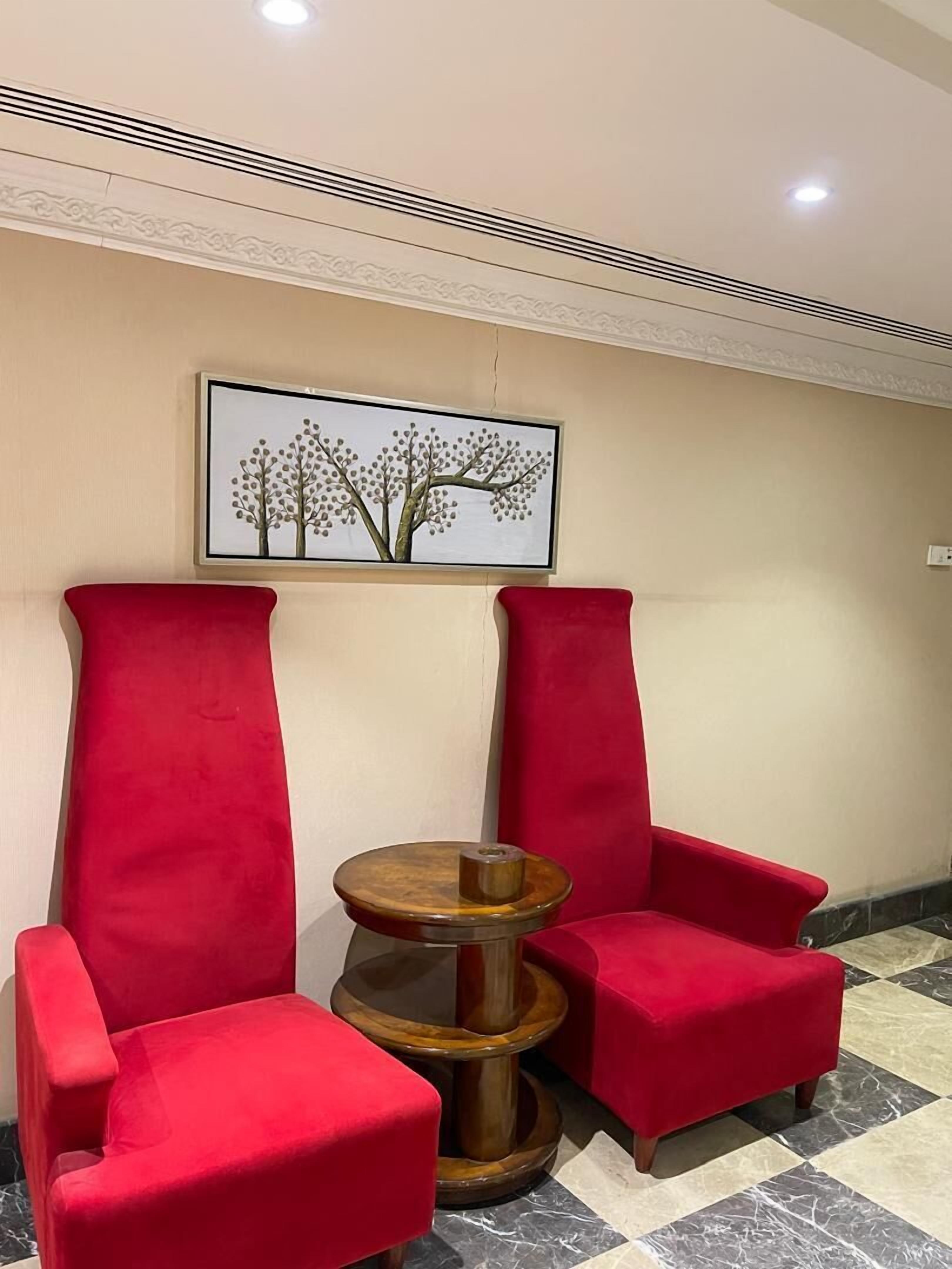 Una habitación con dos sillones rojos, una mesita de madera y un cuadro enmarcado con un paisaje de árboles.