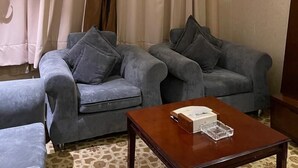 Ein Hotelzimmer mit zwei grauen Sofas, einem Holztisch und einem großen Fenster mit Vorhängen.