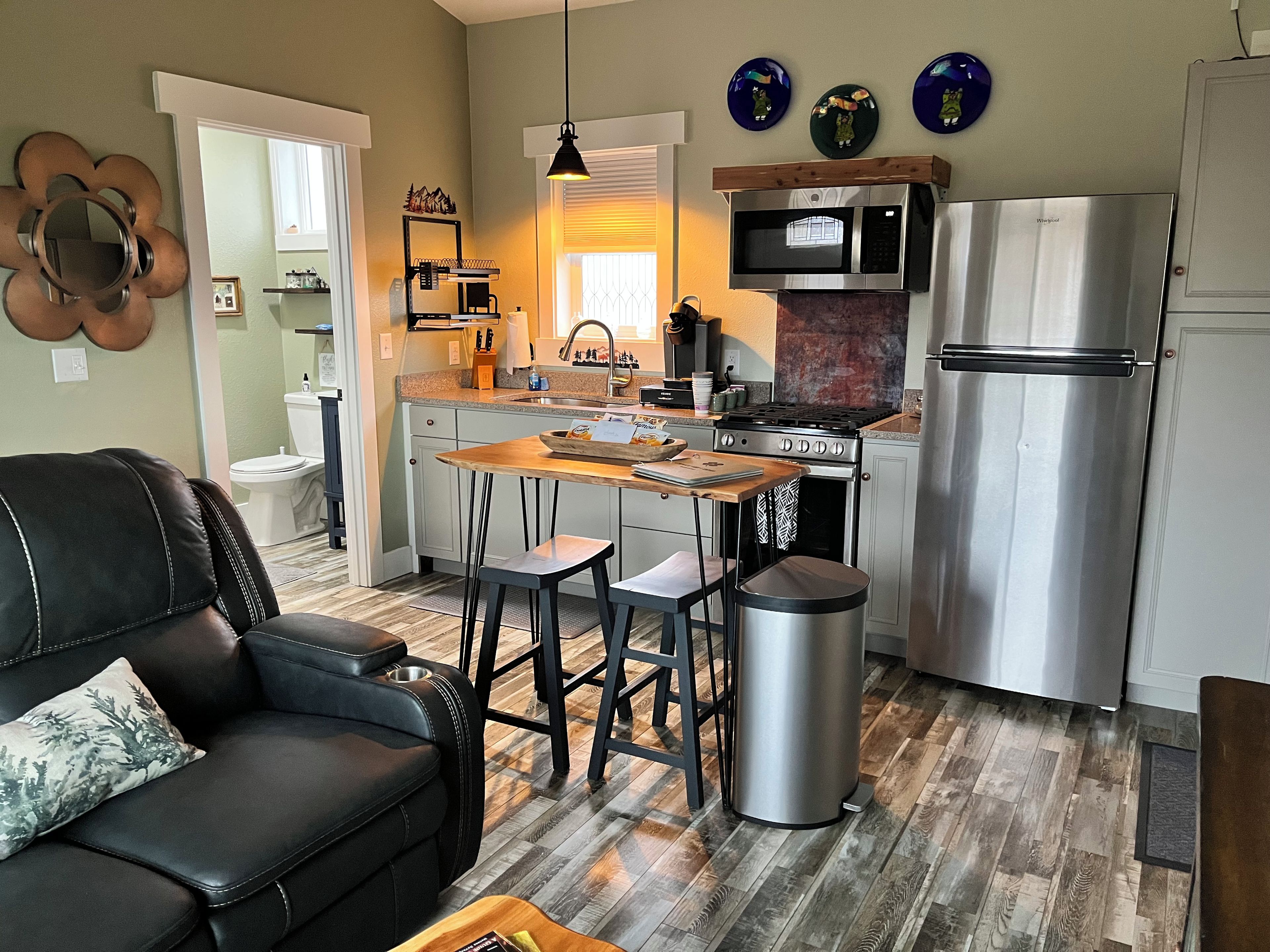 A modern kitchen with a dining area, stainless steel appliances, and a black leather sofa.