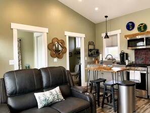 Una cocina moderna con una isla central, un comedor con sofá de cuero negro y vistas al salón.