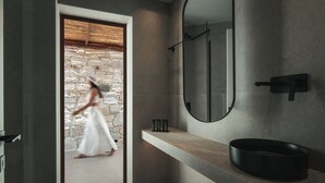 Un bagno moderno con una parete in pietra, un grande specchio e un lavandino nero.