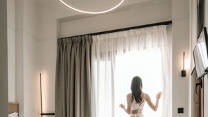 Moderni hotellihuone, jossa on suuri sänky, työpöytä ja suuri ikkuna, jossa on verhot.
