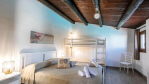 A bedroom with a bunk bed, a bedside table with a lamp, a chair, and a wall with a floral decoration.