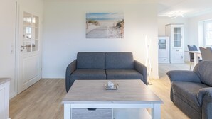 A modern living room with a grey sofa, a wooden coffee table, and a painting of a beach scene on the wall. - Ferienwohnung Schöne Aussicht in Emmelsbüll-horsbüll (Emmelsbüll-Horsbüll)