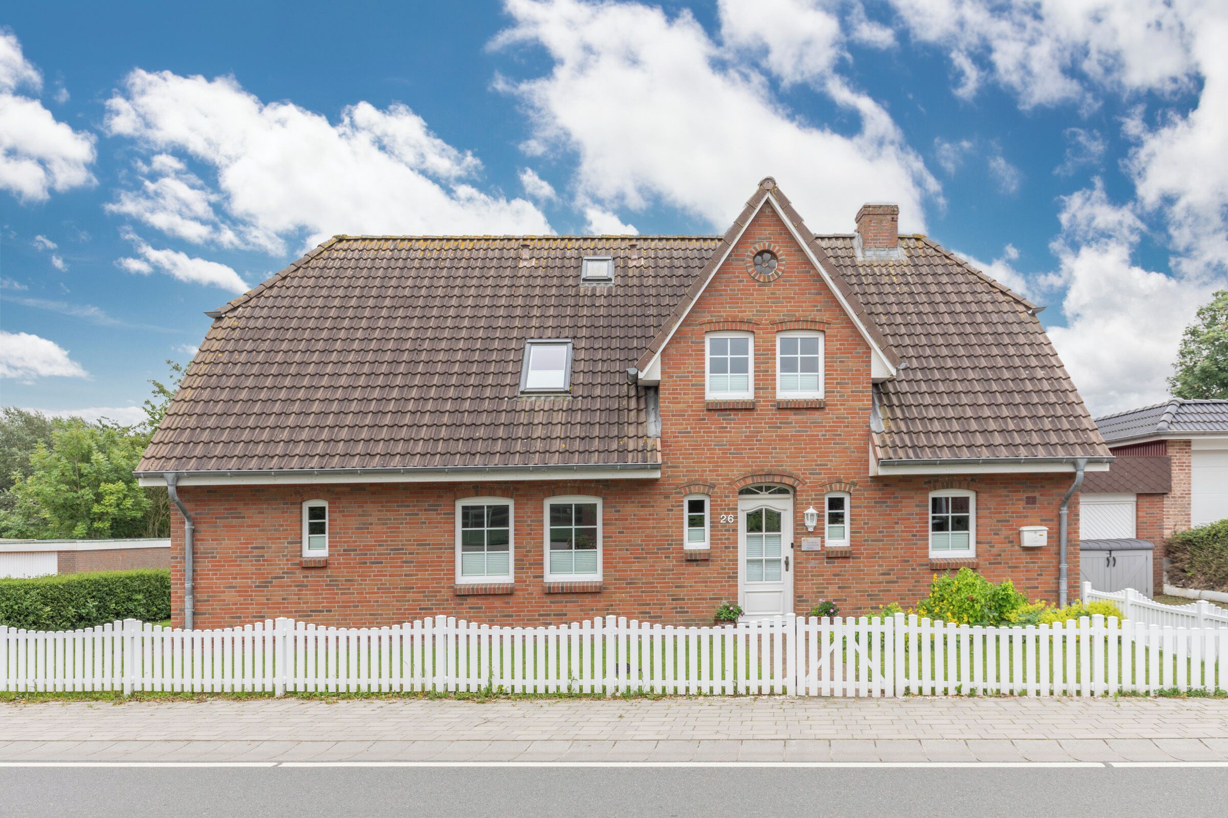 A two-story brick house with a white picket fence, a tiled roof, and a small porch.