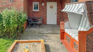 A brick patio with a wooden play area, a white door, and a wicker sofa.