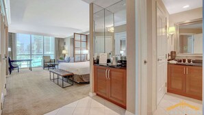 A hotel room with a large bed, a sitting area with a bench, a dining table, and a view of the city. - MGM Signature | Jacuzzi, Strip View & Kitchenette (Las Vegas)