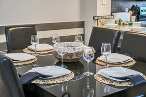 A dining table set with white plates, silverware, and wine glasses, surrounded by black chairs. - Family Townhouse near Disney (Kissimmee)