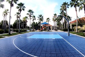 A basketball court with a blue surface, surrounded by palm trees and a gazebo in the background. - Family Townhouse near Disney (Kissimmee)