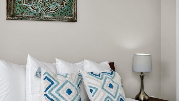 Un lit bien fait, avec une literie blanche et des coussins décoratifs ornés de motifs géométriques.