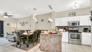 Une cuisine moderne avec des meubles blancs, un îlot en granit, des appareils en acier inoxydable et des luminaires suspendus.