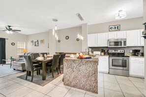 A modern kitchen with white cabinets, a granite island, stainless steel appliances, and pendant lighting. - Family Townhouse near Disney (Kissimmee)