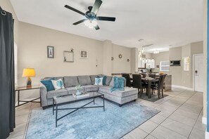 A living room with a gray sectional sofa, a coffee table, and a dining area with a table and chairs. - Family Townhouse near Disney (Kissimmee)
