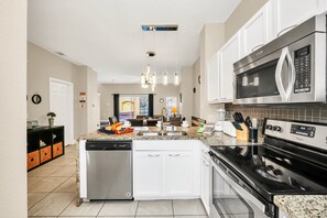 A modern kitchen with white cabinets, stainless steel appliances, and a granite countertop. - Family Townhouse near Disney (Kissimmee)