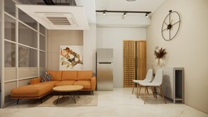 A modern living room with a sectional sofa, a round coffee table, and a white armchair. There is a painting on the wall, a wooden door, and a white cabinet. - Apartment De Thamel  (Kathmandu)