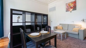 A modern living room with a dining area, a sofa, and a bookshelf. - Cozy Studio in Central Porto: A/C and Kitchen (Porto)