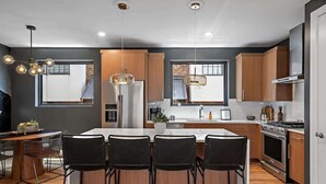 Una cocina moderna con armarios de madera, una isla central con taburetes de bar, electrodomésticos de acero inoxidable e iluminación colgante.