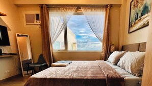 A hotel room with a large bed, a desk, a chair, and a window with curtains. - Hubomoto Megaworld Suites (Iloilo)