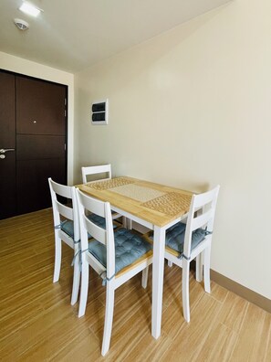 A dining area with a wooden table and white chairs, a dark door, and a light switch on the wall. - Hubomoto Megaworld Suites (Iloilo)