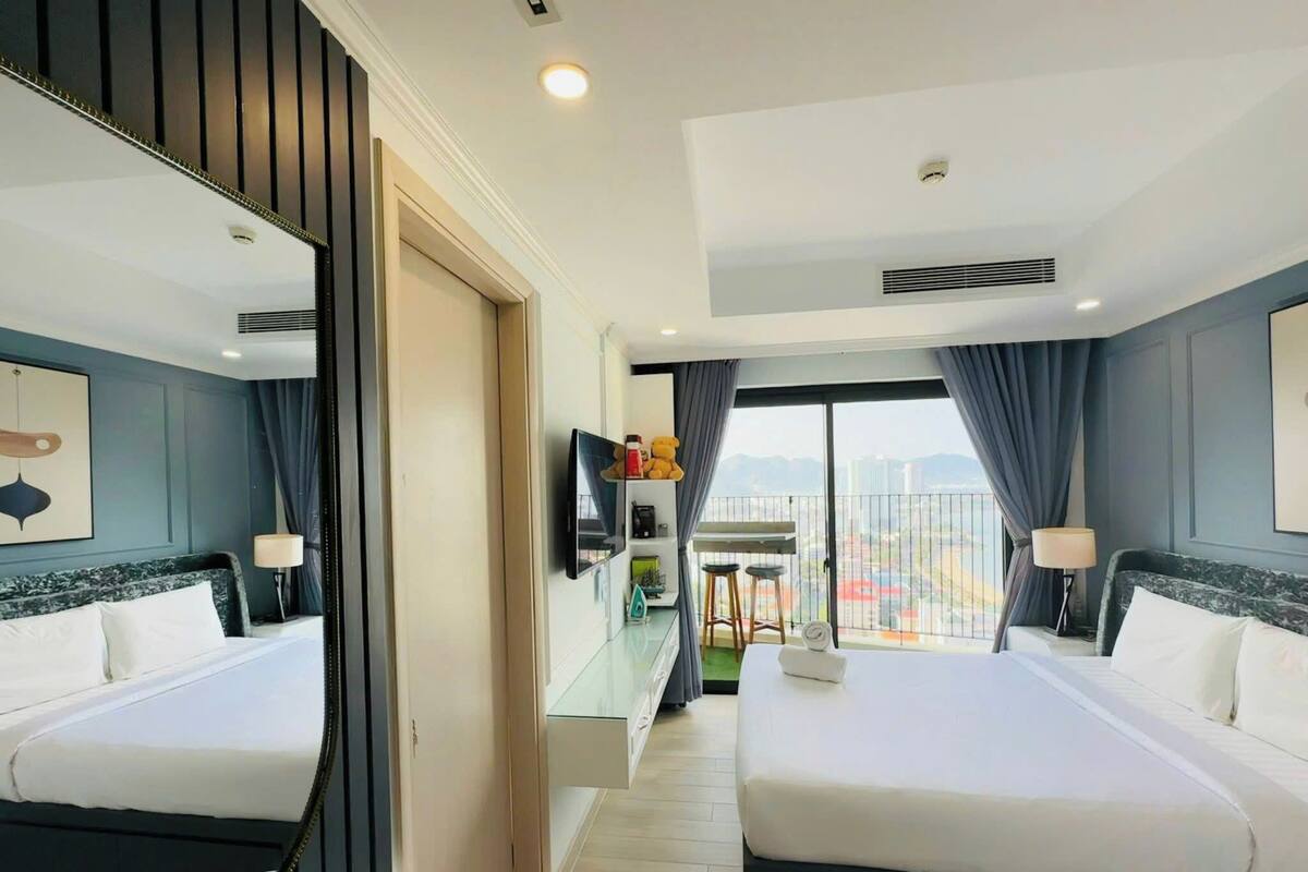 A hotel room with two beds, a large mirror, a TV, a balcony with a view, and a small table with stools.