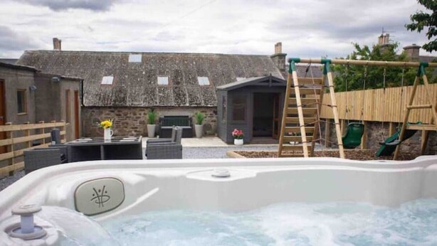 Un bain à remous dans un jardin, avec un bâtiment en pierre, une clôture en bois et une échelle.