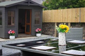 A small wooden cabin with a door, two potted plants with pink flowers, and a table with a vase of yellow flowers. - Formerly the Crannoch Hotel, this wonderful property can sleep up to 18
 (Cullen)