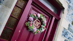 Une porte rouge ornée d’une guirlande de fleurs et d’une plaque dorée.