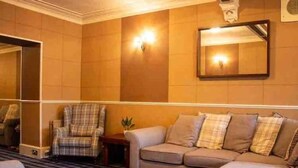 Une chambre d’hôtel avec un sol à carreaux, un canapé agrémenté de plusieurs coussins, un fauteuil à motifs écossais et un miroir au mur.