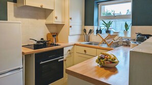Une cuisine moderne avec des armoires blanches, un plan de travail en bois, un four encastré et une fenêtre donnant sur des maisons.