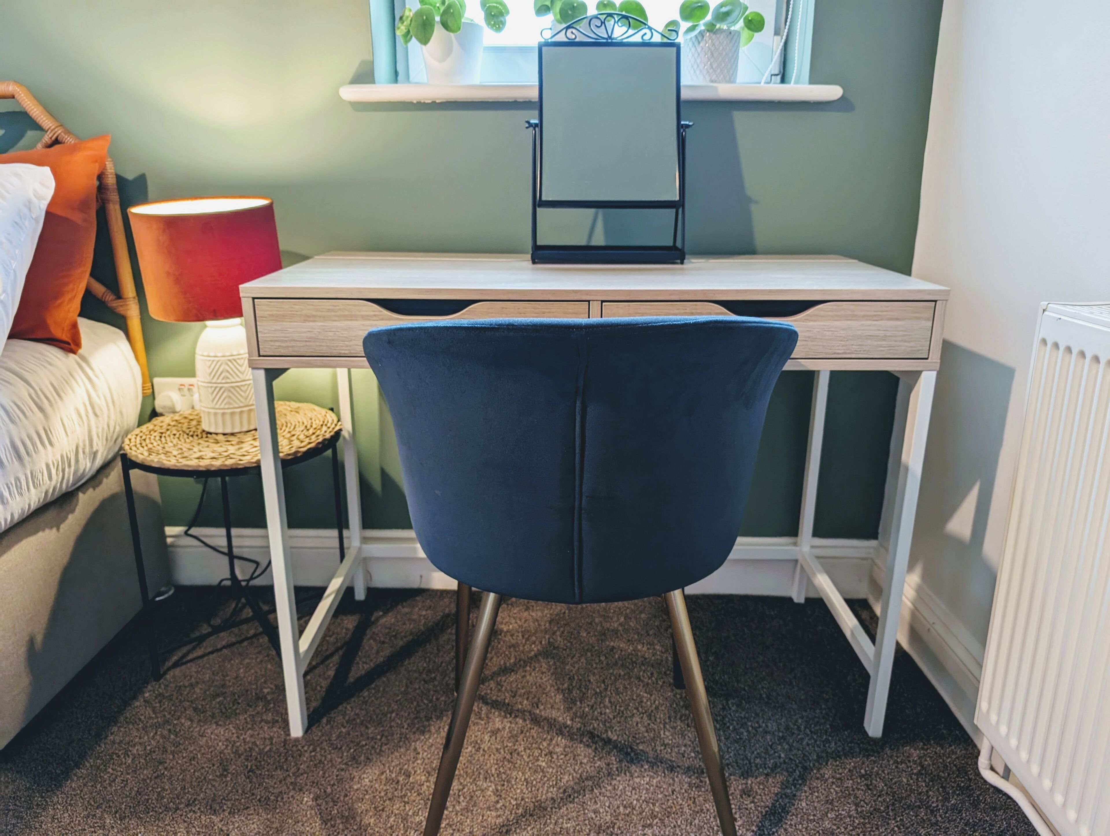 Een kamer met een bureau, een stoel, een lamp, een bijzettafeltje en een radiator.