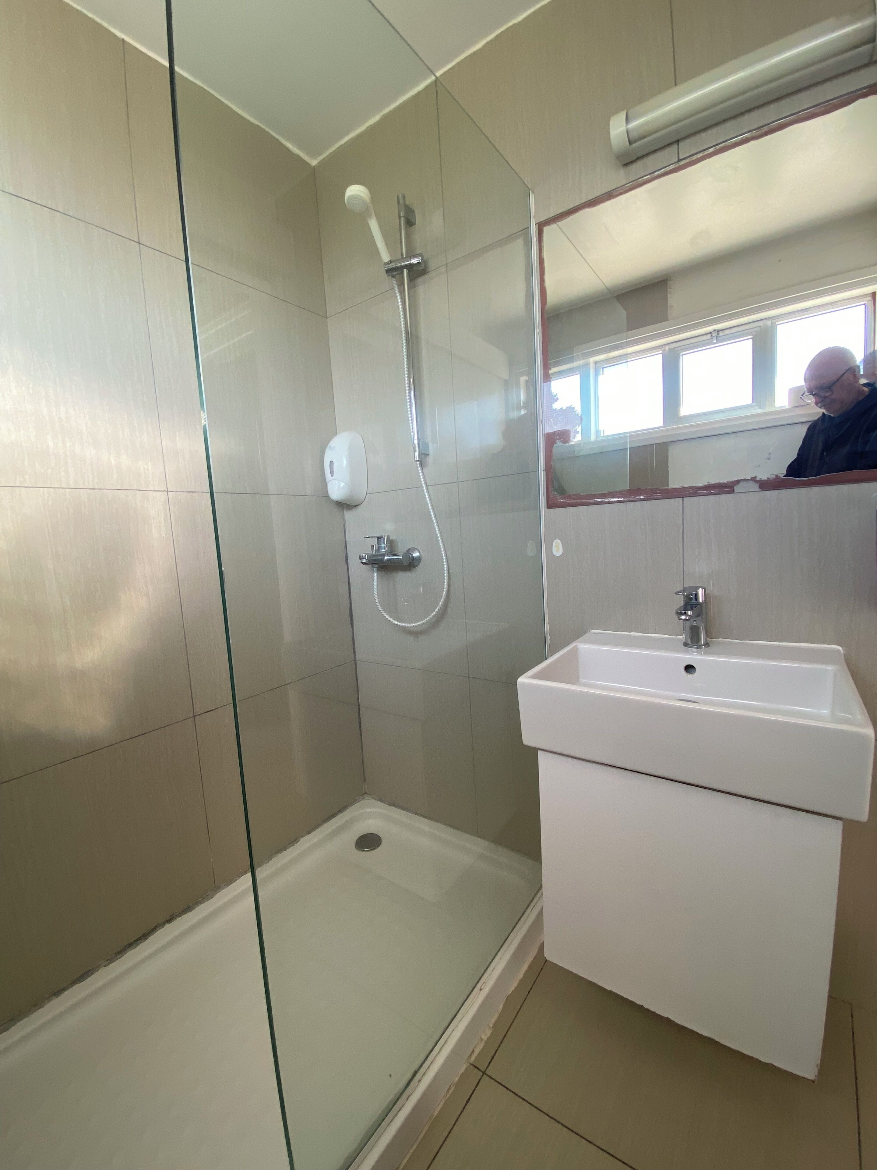 Un baño moderno con ducha de vidrio, lavamanos blanco y espejo sobre el lavamanos.