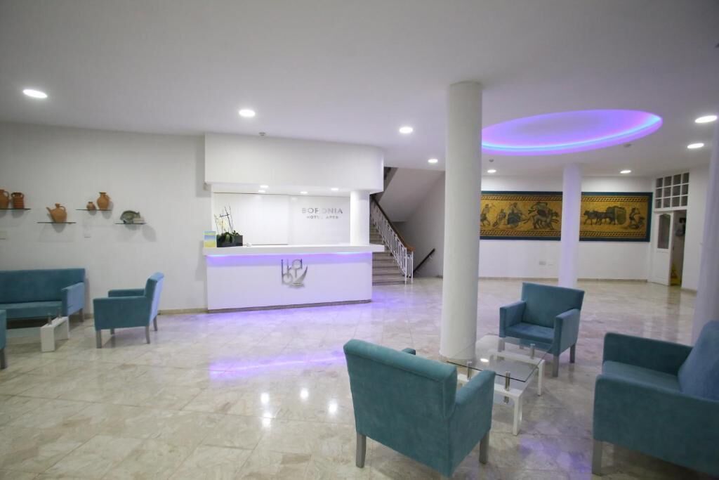 Un vestíbulo moderno con una recepción, sillas color turquesa y una escalera.