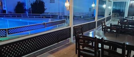 An outdoor dining area with a pool view, wooden tables, and chairs.
