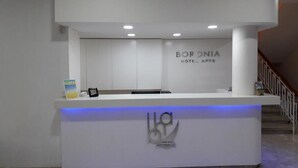 Een receptiebalie van een hotel met een modern design, met een logo en de naam 'BORONIA HOTEL APTE'.