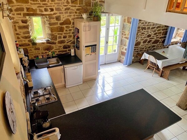A kitchen with a stone wall, a refrigerator, a stove, and a dining area with a table and chairs.